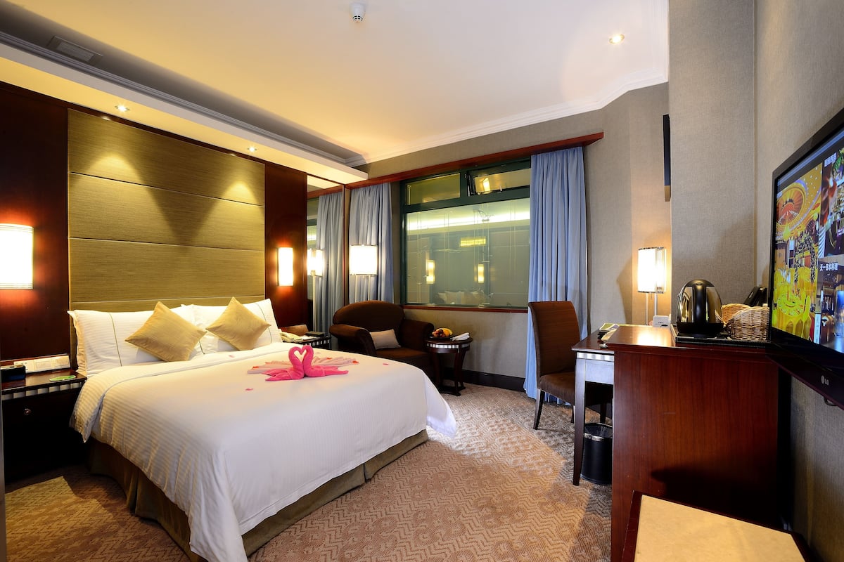 Una habitación de hotel con una cama grande, un escritorio, una silla, un televisor y una ventana con cortinas.