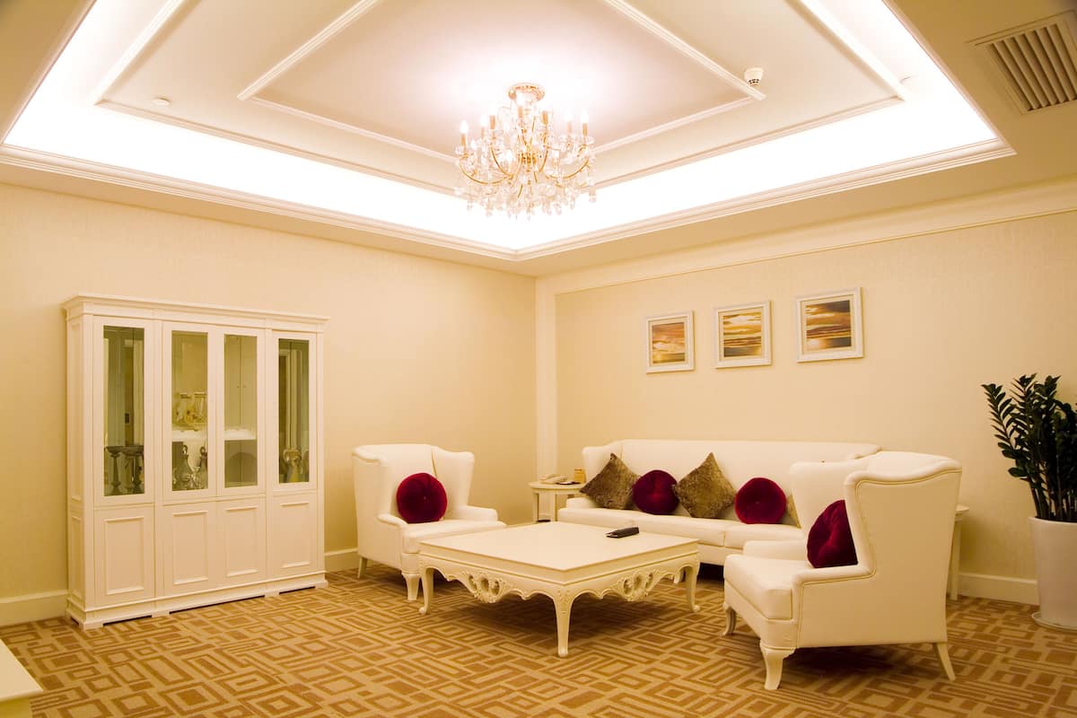 Un salón luminoso con un sofá blanco, sillones a juego, una mesa de centro y un aparador con puertas de cristal.