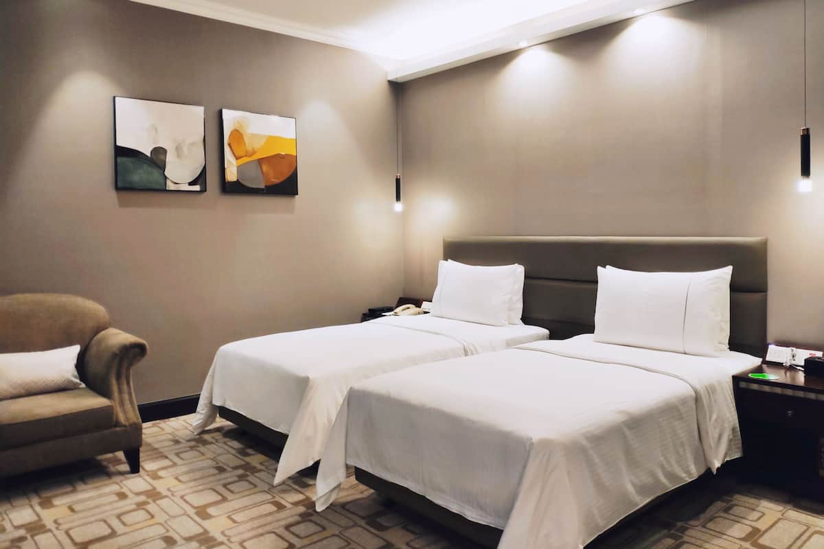 Habitación de hotel con dos camas, un sofá y dos cuadros abstractos en la pared.