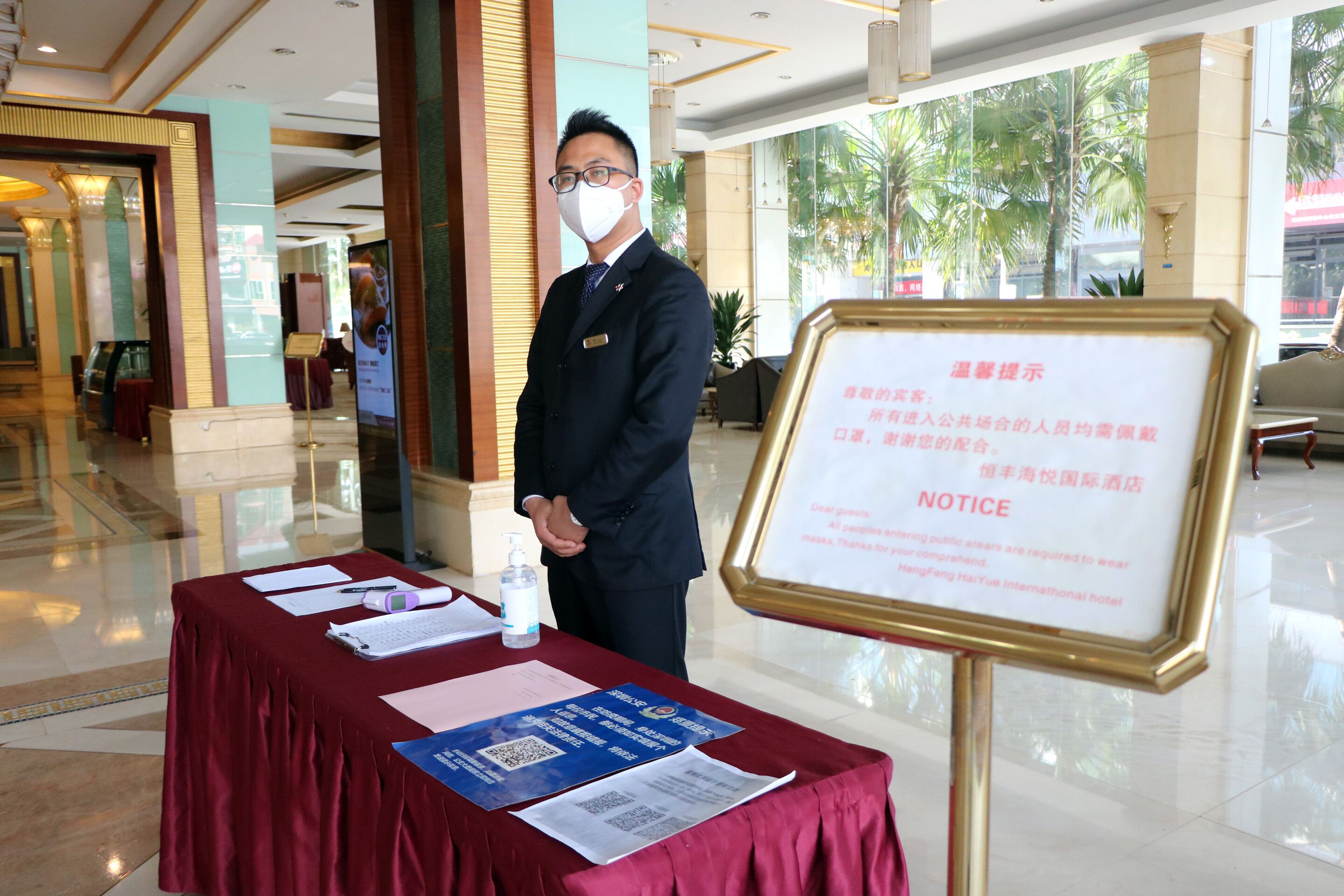 A hotel lobby with a man standing by a table with papers and a notice board.