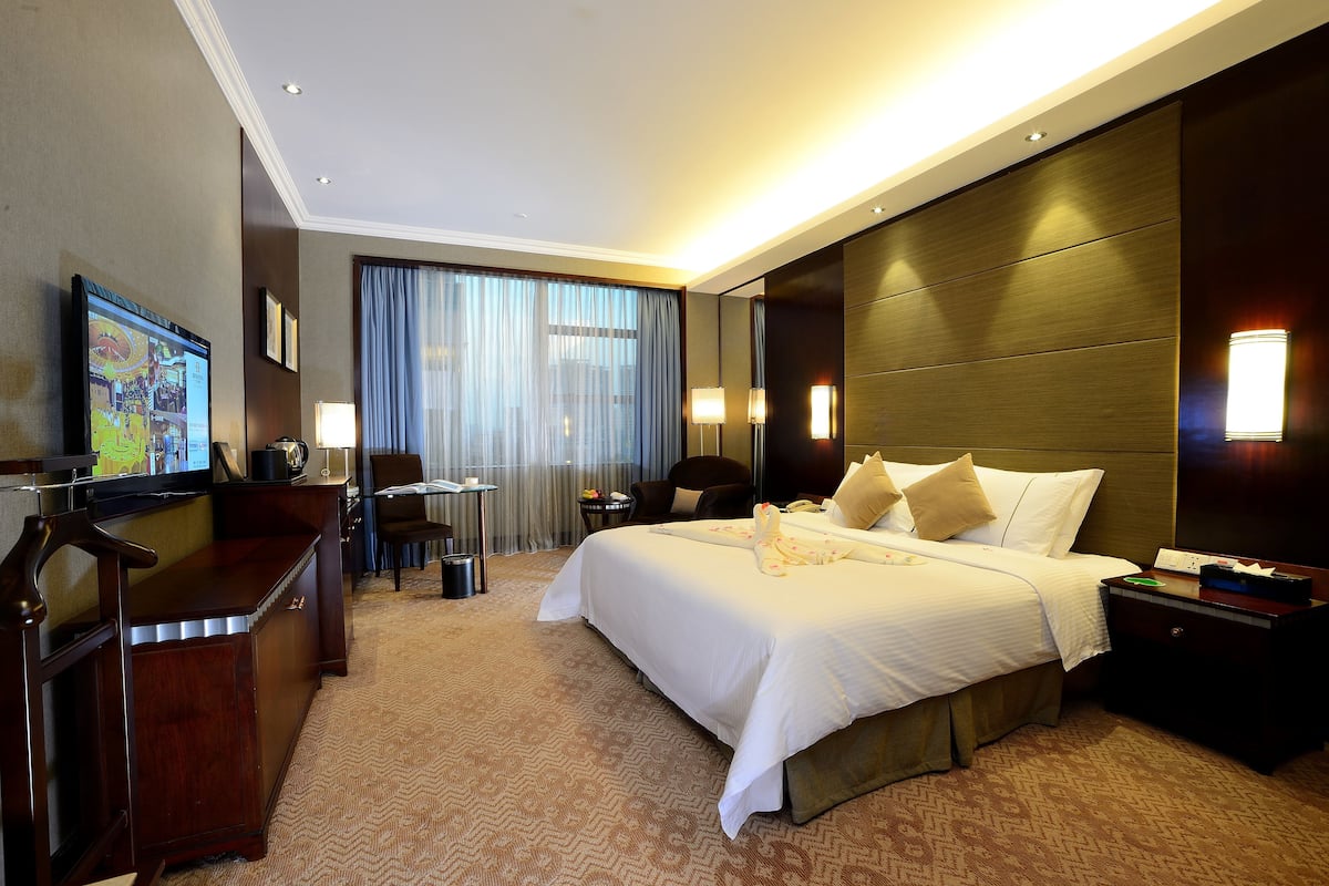 Una habitación de hotel con una cama grande, un escritorio, una silla, un televisor y una ventana con cortinas.