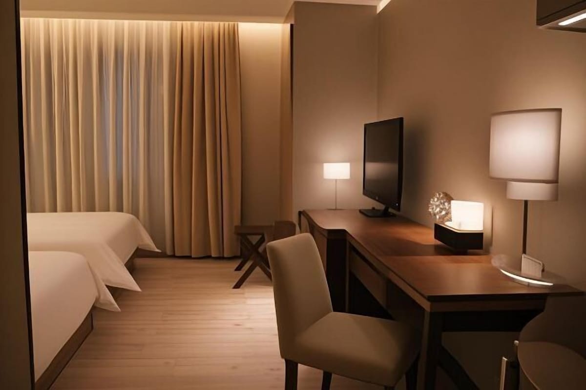 Una habitación de hotel con cama, escritorio con televisor, una silla y una lámpara.