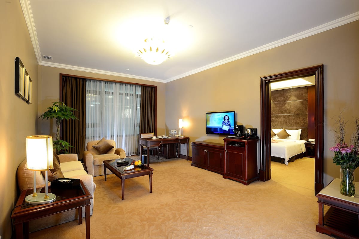 Habitación de hotel con sala de estar, televisor, escritorio, cama y baño visible a través de una puerta abierta.