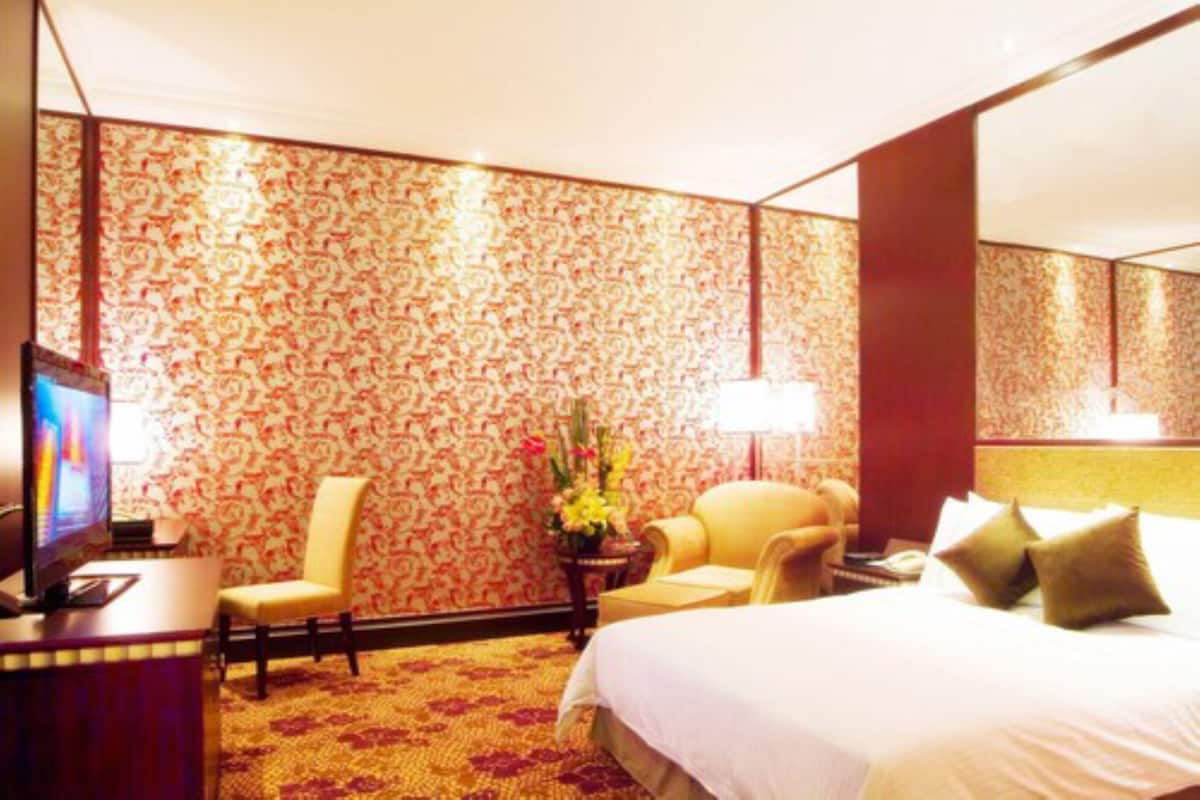 Una habitación de hotel con una cama grande, un escritorio con televisión, una silla y una pequeña mesa con flores.