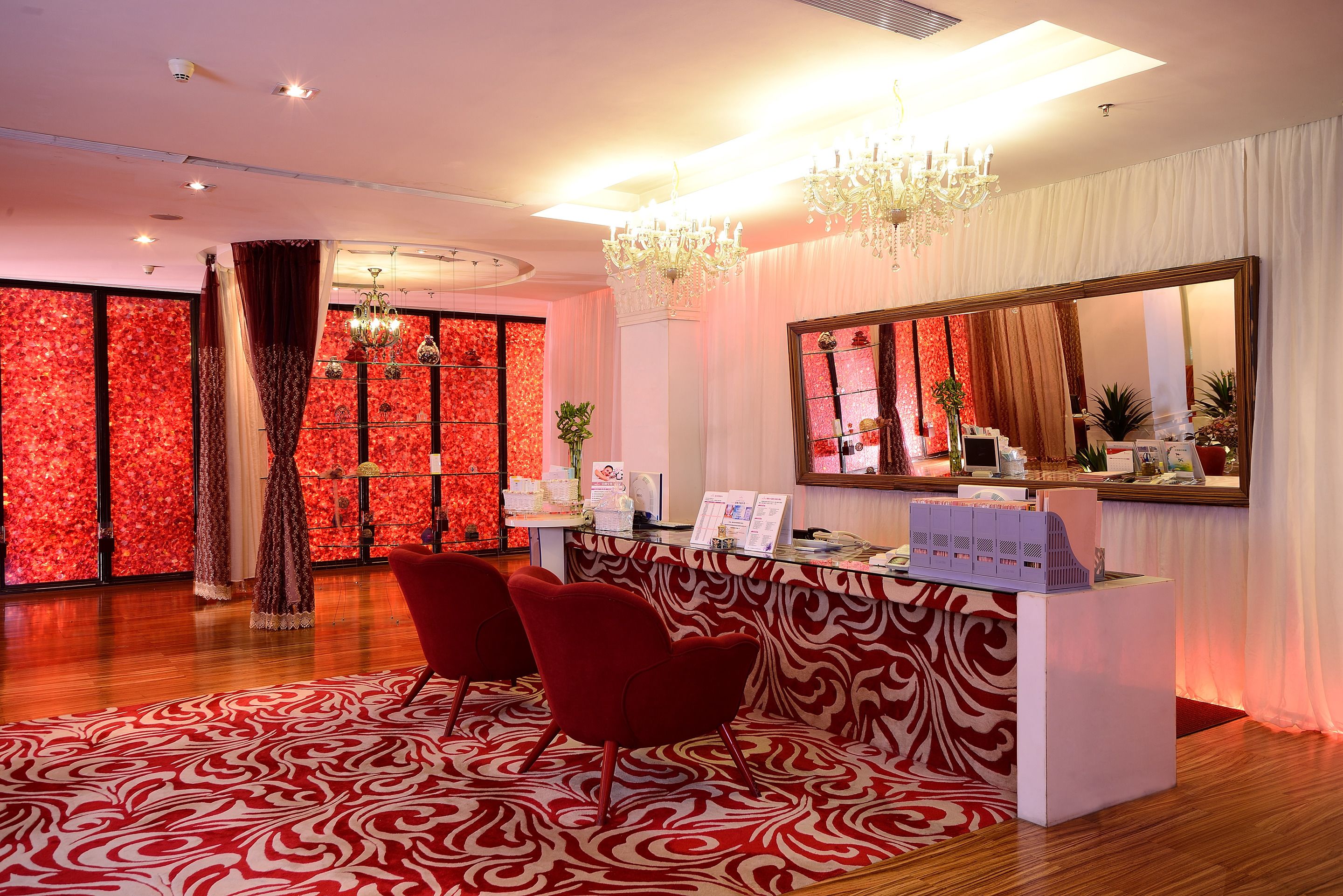 A reception area with a red and white patterned carpet, a reception desk with a mirror, and a chandelier.