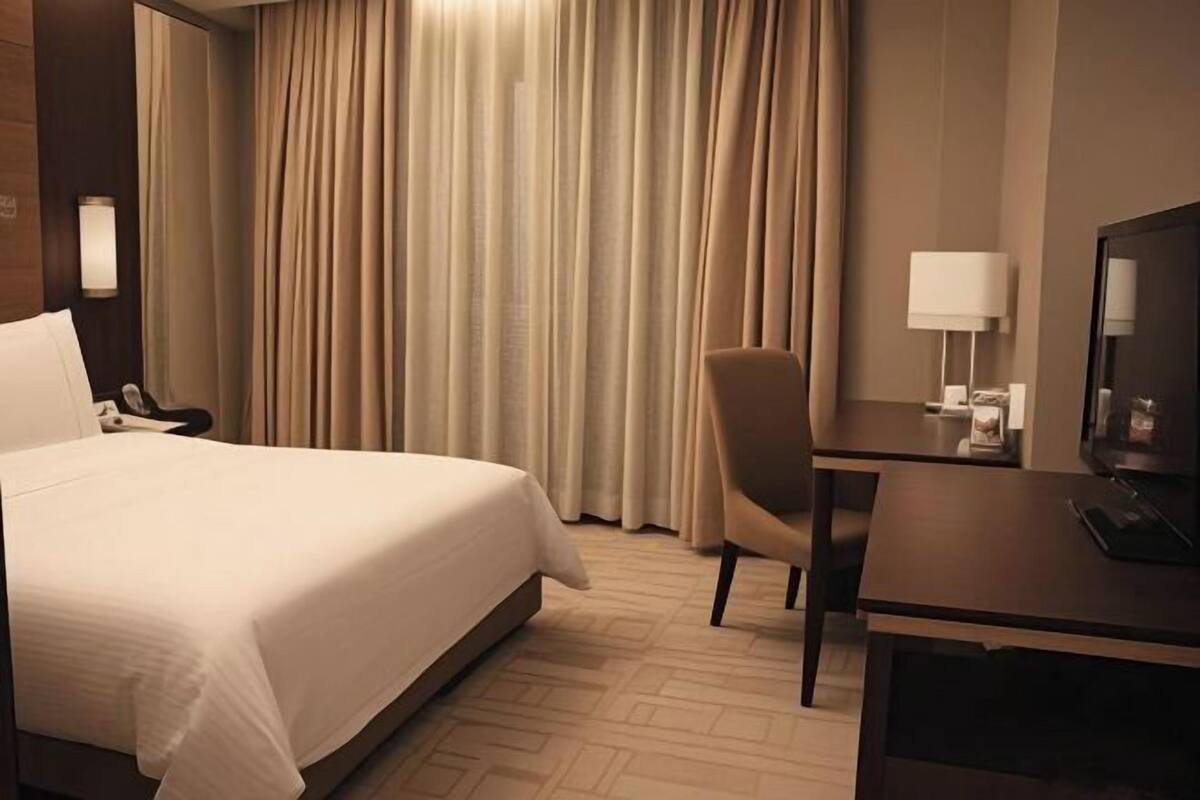A hotel room with a bed, a desk, a chair, a television, and curtains.