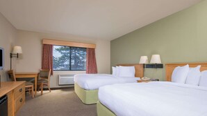 A hotel room with two beds, a desk, a chair, a lamp, and a window with curtains.