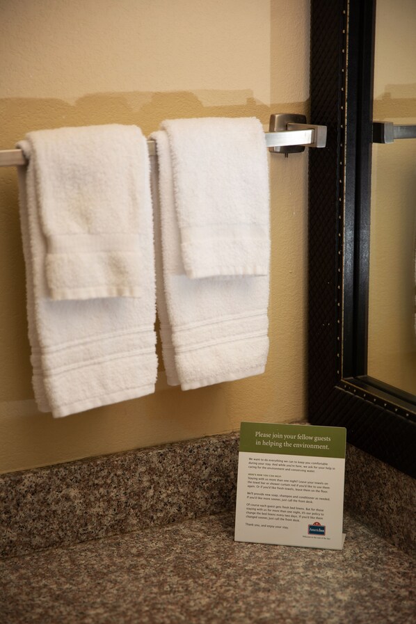 A bathroom with two white towels hanging on a towel rack, a granite countertop, and a sign with environmental conservation information.
