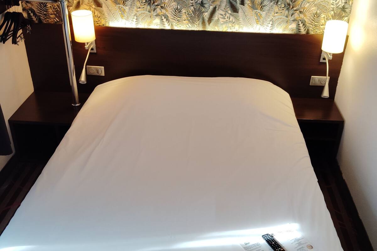 A hotel room with a large bed, two bedside tables with lamps, and a wall with a leaf pattern.