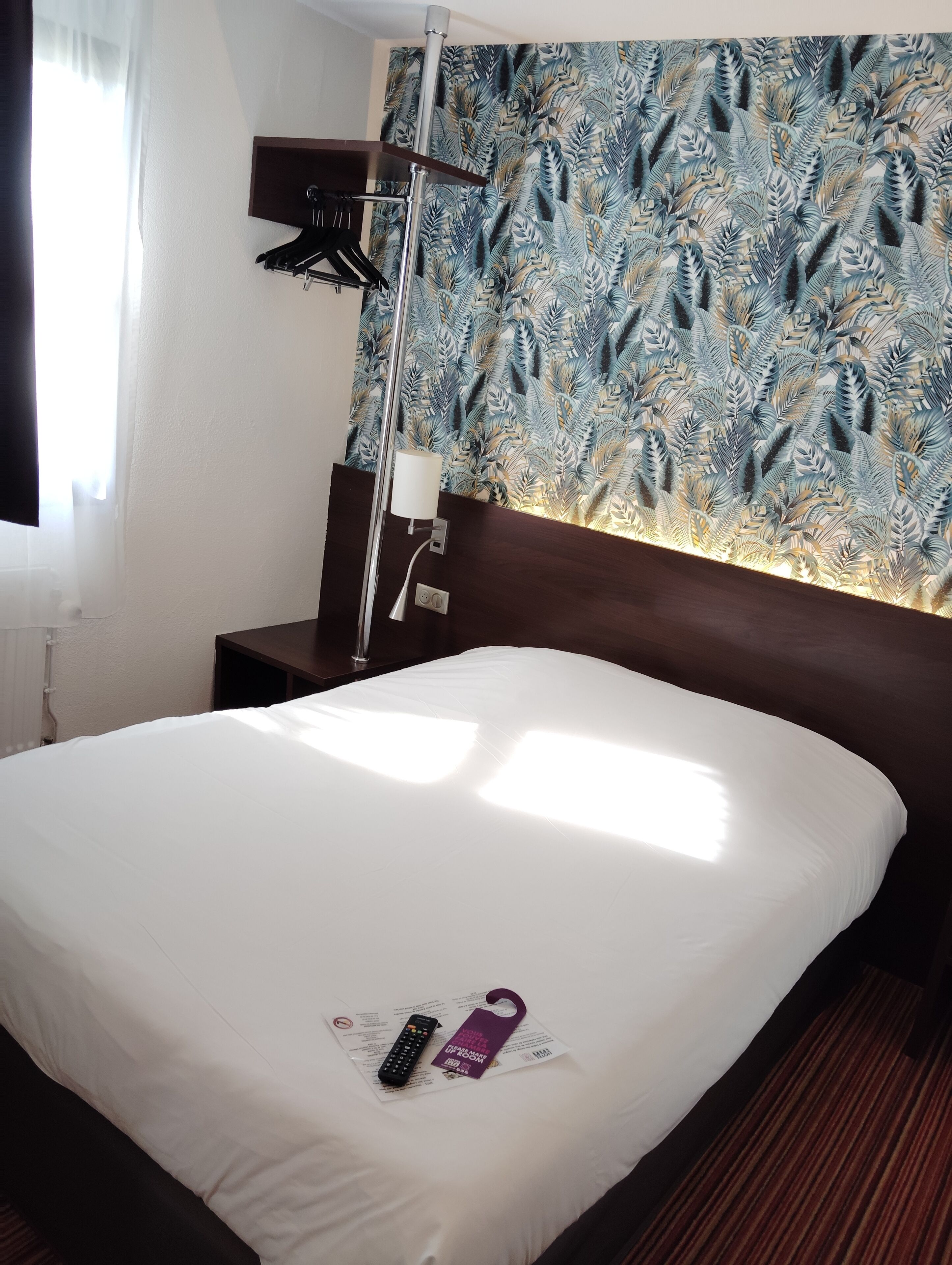 A hotel room with a bed, a nightstand, a lamp, and a wall with a leaf pattern.