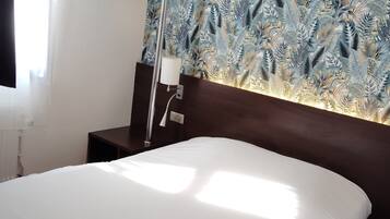 Quarto de hotel com uma cama, mesa de cabeceira, abajur e parede com padrão de folhas.