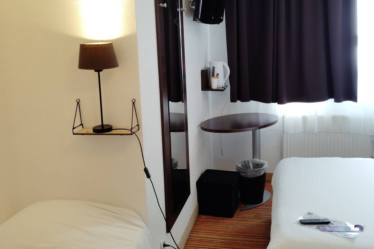A hotel room with a bed, a bedside table, a lamp, a TV, and a window with curtains.