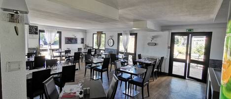 A spacious dining area with multiple tables and chairs, a chalkboard menu, and a clock on the wall.