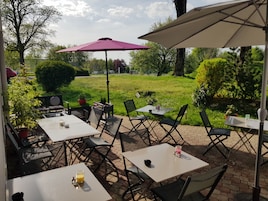Un patio al aire libre con mesas y sillas, rodeado de follaje y árboles.