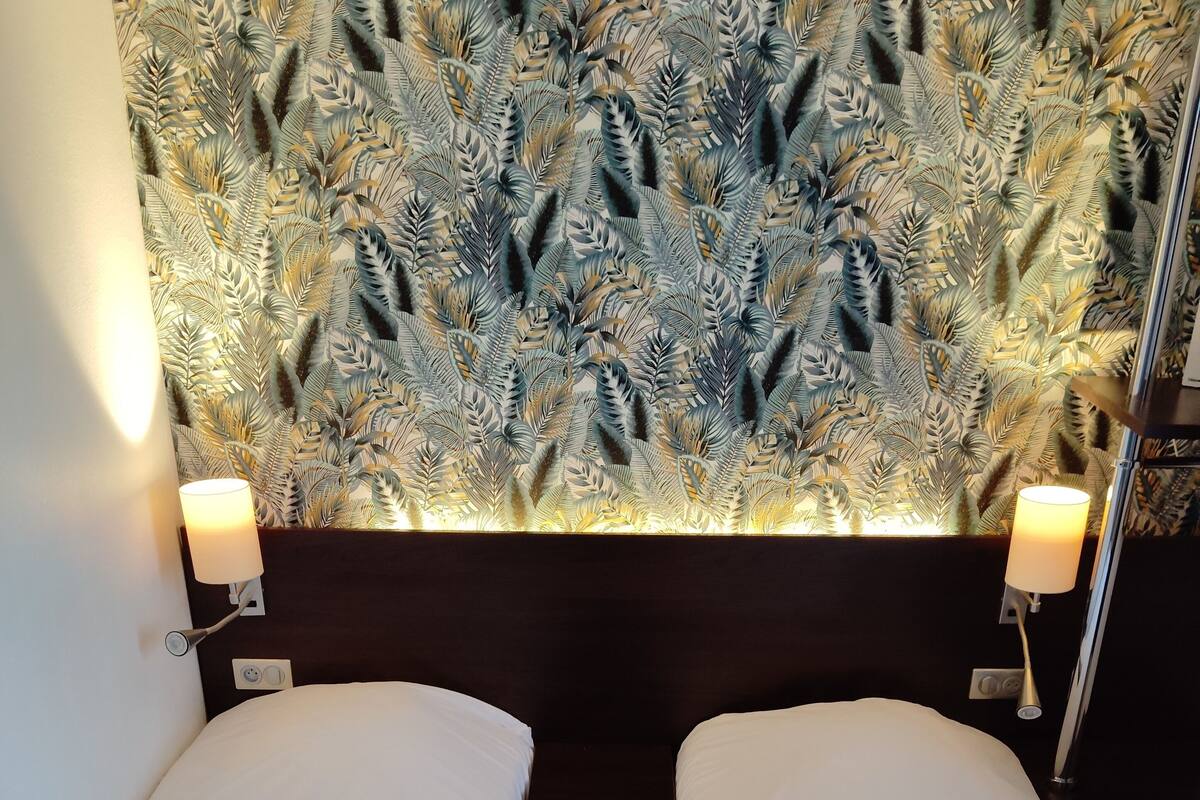 A hotel room with two single beds, a patterned headboard, bedside lamps, and a remote control on one bed.