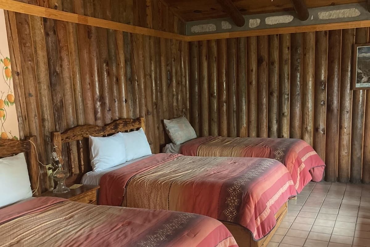 A rustic wooden room with three beds, each with a patterned bedspread, and a tiled floor.
