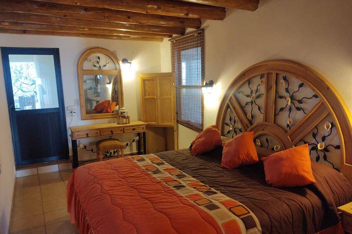 A bedroom with a wooden headboard, a bed with orange bedding, a dresser, a mirror, and a window with blinds.