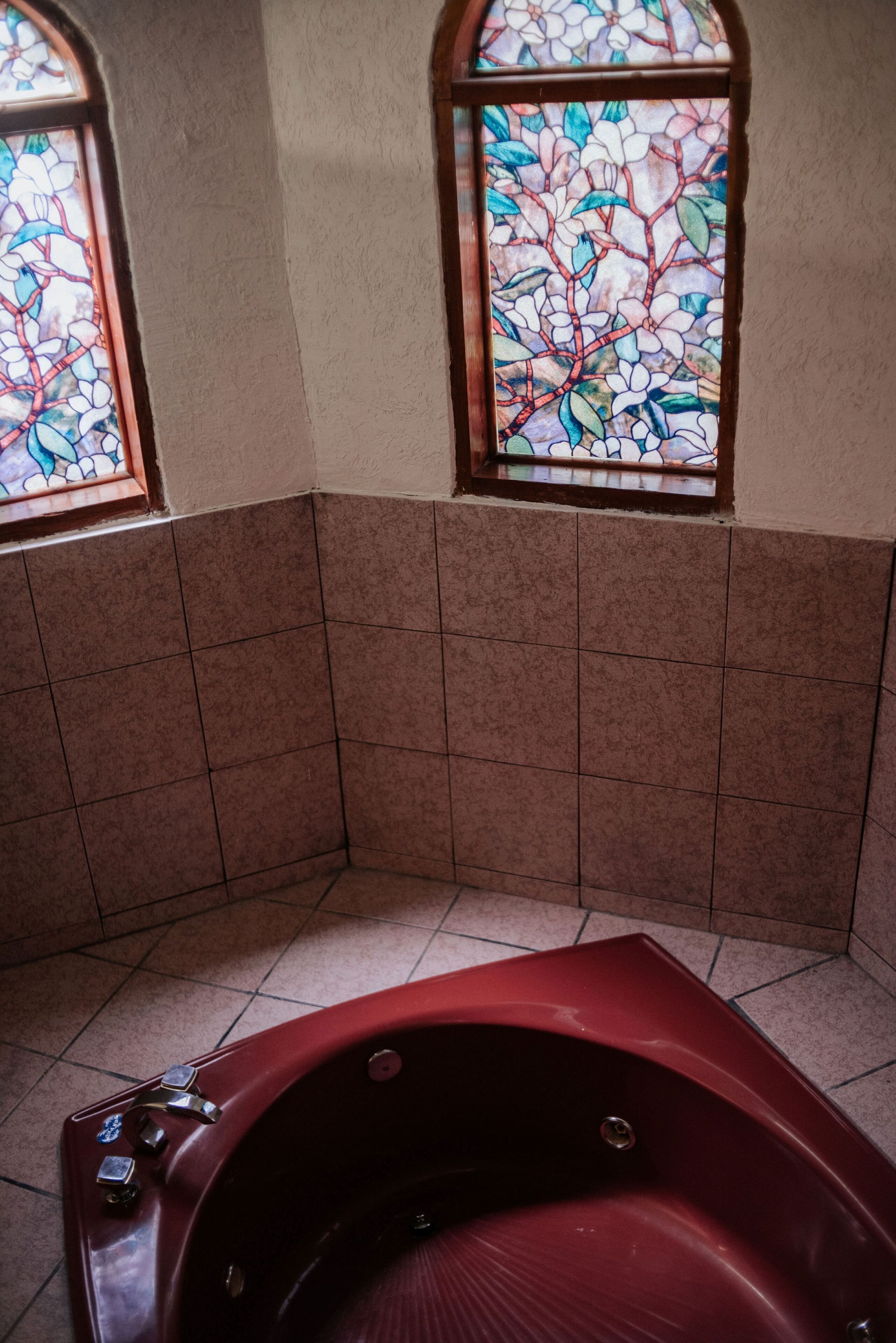 Un baño con una bañera roja, paredes con azulejos y dos ventanas de vitral.