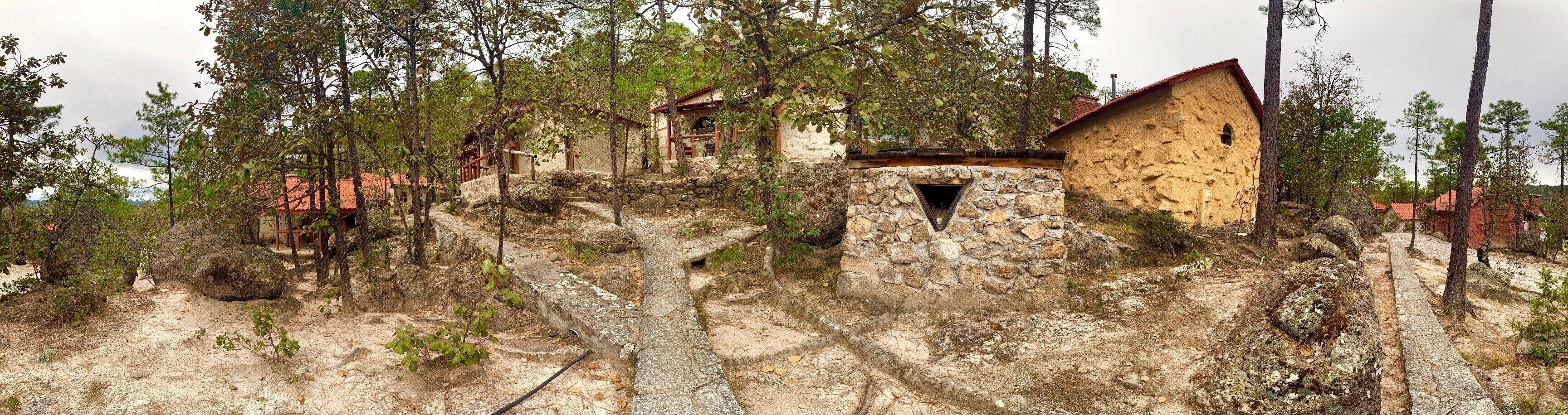 A rustic stone building with a small window and a wooden door, surrounded by trees and a stone pathway.