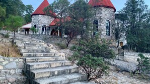 Ein Steinhaus mit roten Dächern und einer Treppe, die davor hinauf führt.