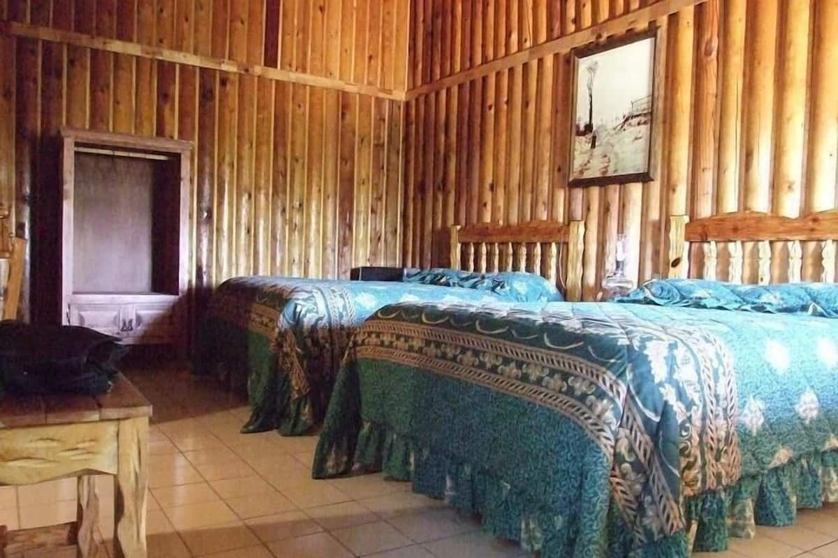 A room with two beds, wooden walls, a tiled floor, and a painting on the wall.