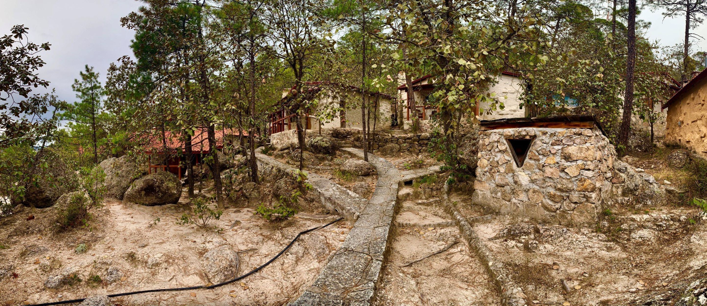 Un edificio rustico in pietra con un vialetto stretto che vi conduce, immerso tra alberi e terreno roccioso.