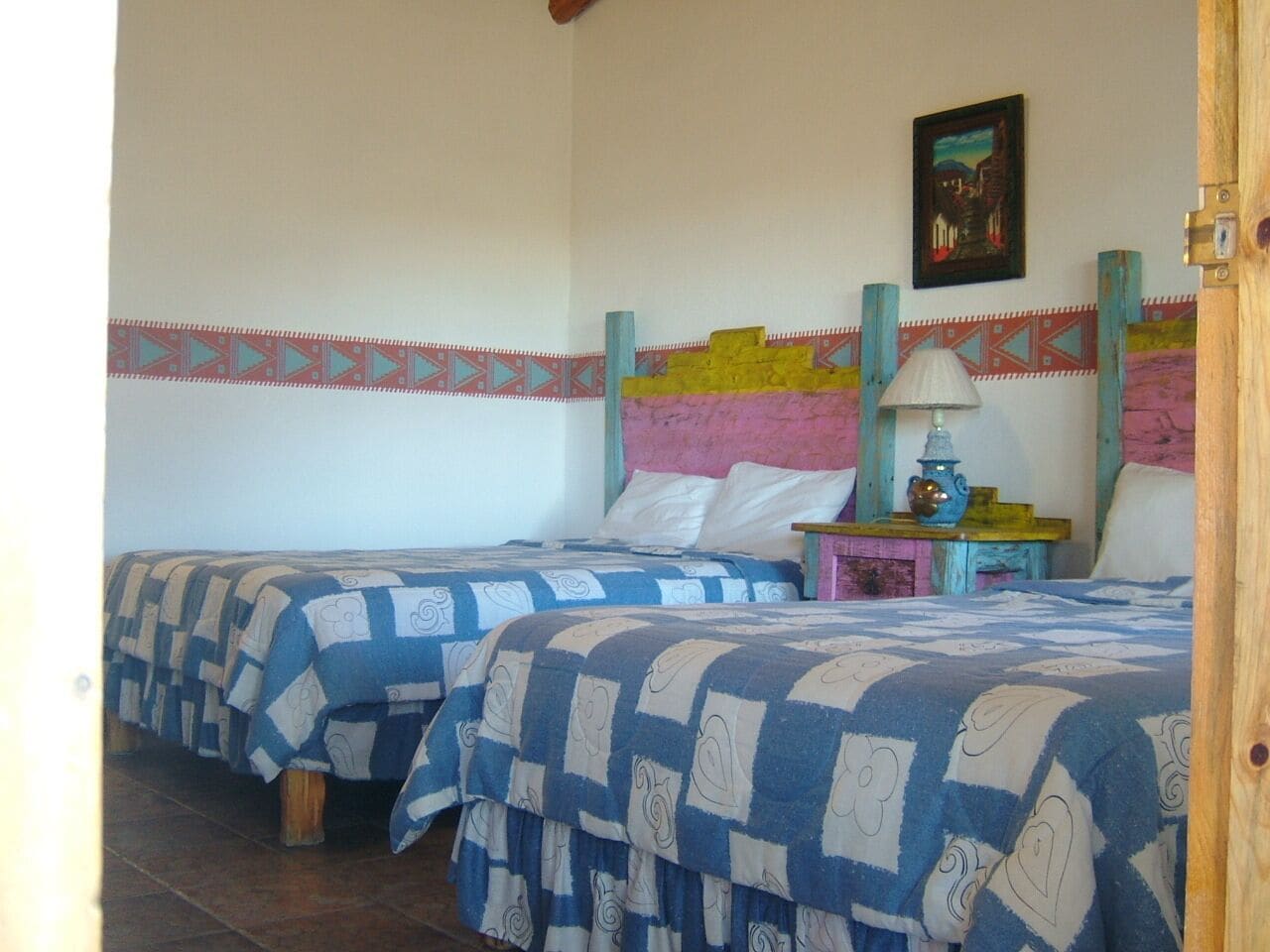 Habitación con dos camas, cada una con una colcha estampada, una mesita de noche con lámpara y un cuadro en la pared.