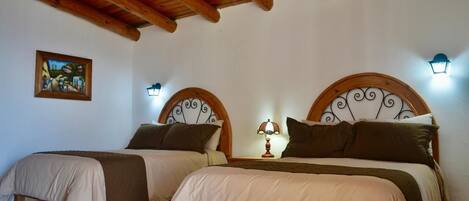 Una habitación con dos camas, vigas de madera en el techo, una lámpara de pared y un cuadro enmarcado.