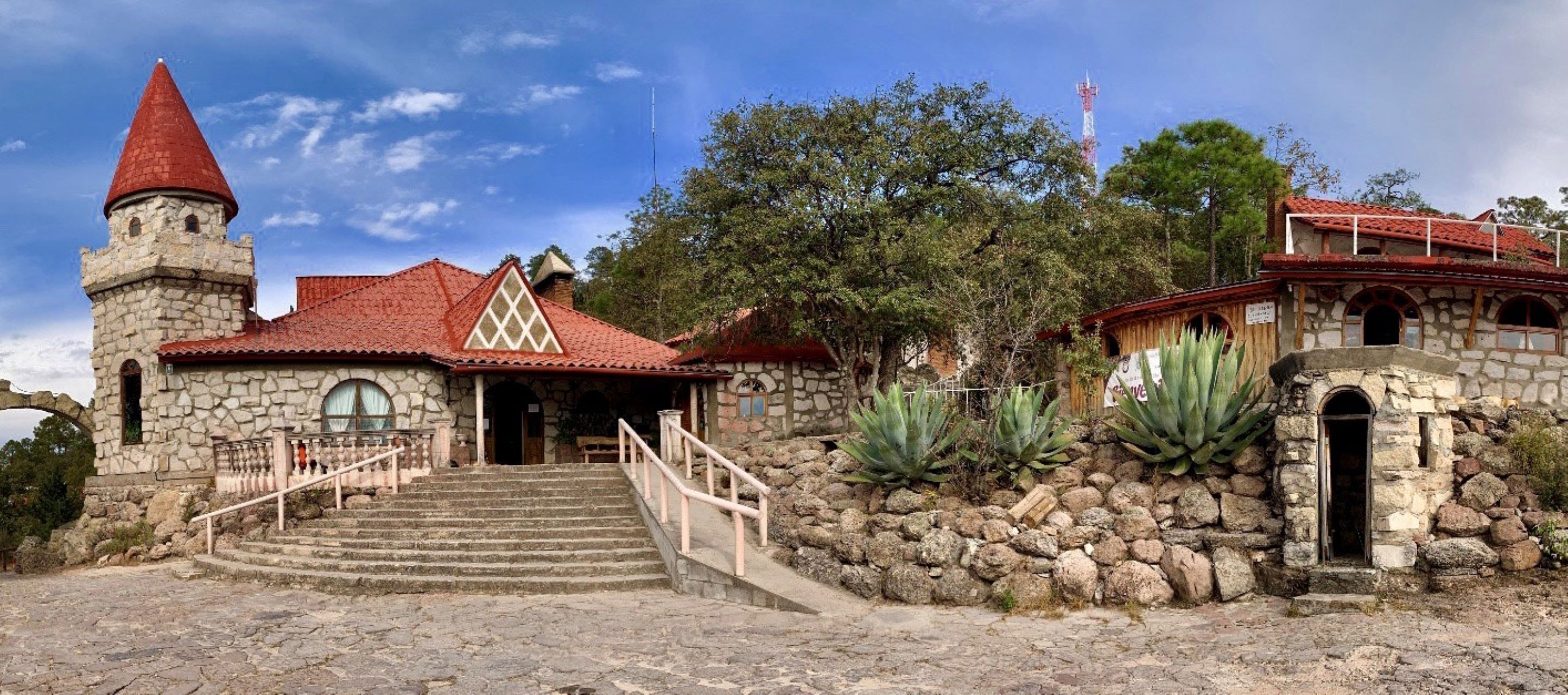 A stone building with a red-tiled roof, a tower, and a staircase leading to the entrance.