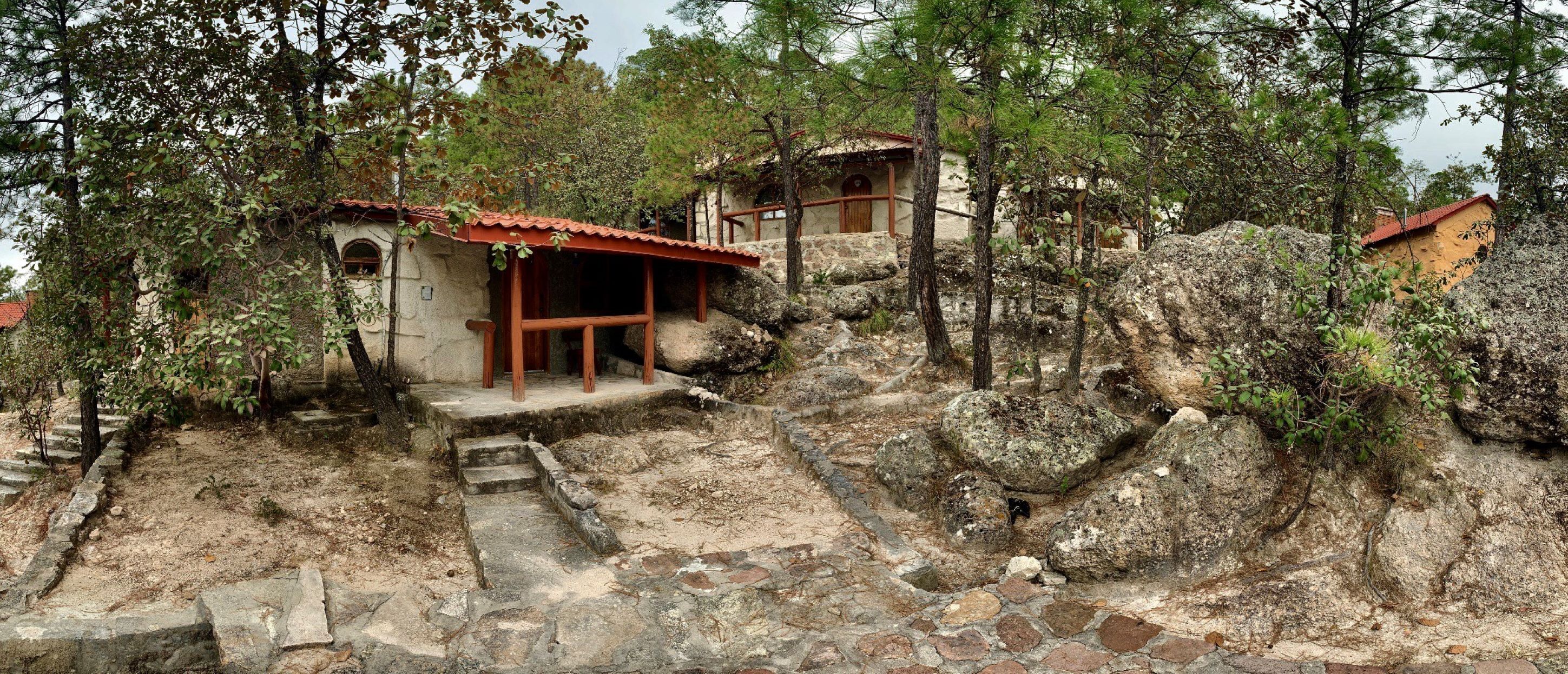 A rustic stone building with a wooden staircase leading to a door, surrounded by trees and rocky terrain.