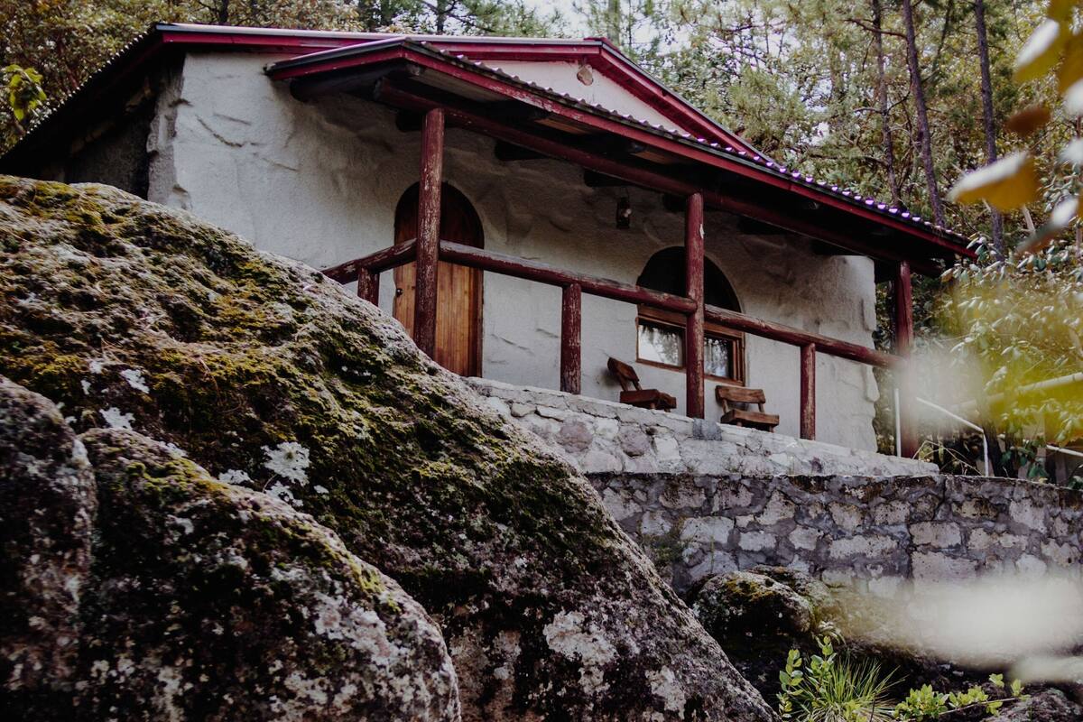 A rustic stone building with a red roof, wooden beams, and a bench outside.