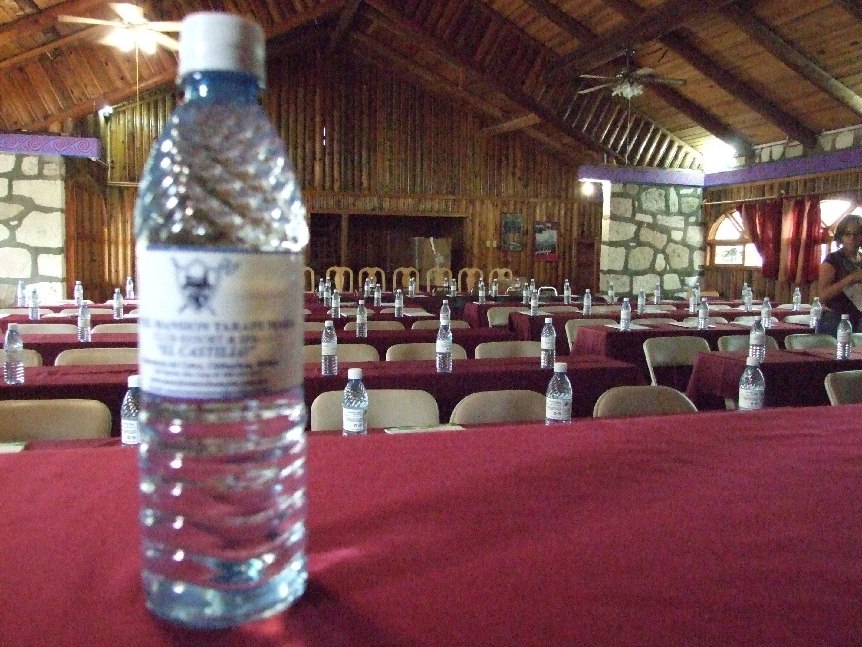 A conference room with tables set up for an event, water bottles on each table, and a wooden ceiling.