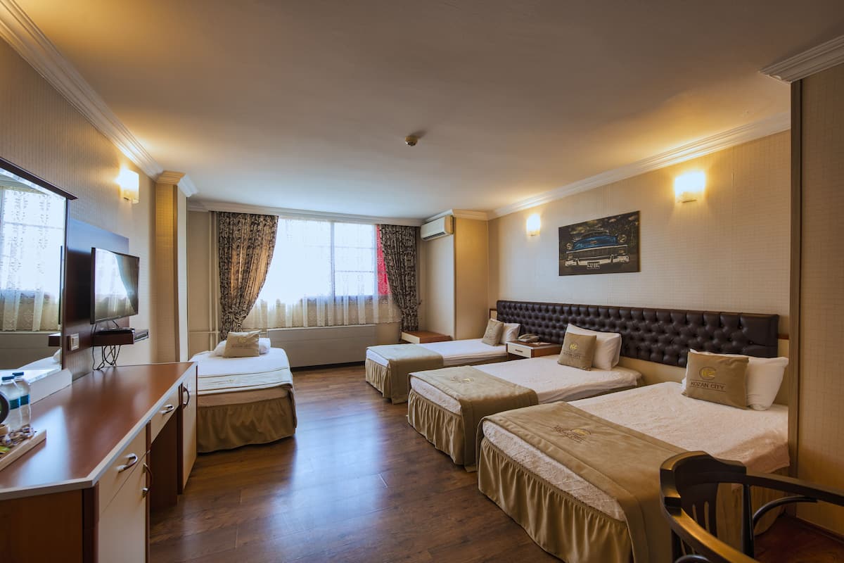 Una camera d'albergo con due letti singoli, un letto matrimoniale, una scrivania con televisione e una finestra con tende.