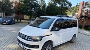 Una camioneta blanca estacionada en un área pavimentada, con árboles y edificios al fondo.