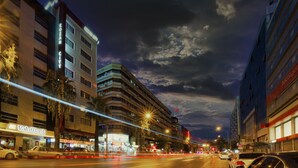 Una calle urbana iluminada de noche, con edificios, farolas y vehículos.