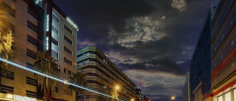 Una calle urbana iluminada de noche, con edificios, farolas y vehículos.