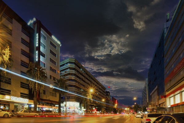 A city street at night with buildings, streetlights, and vehicles.