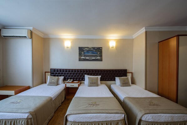 Habitación de hotel con dos camas individuales, un cabecero grande y acolchado, una mesita de noche y un aire acondicionado instalado en la pared.