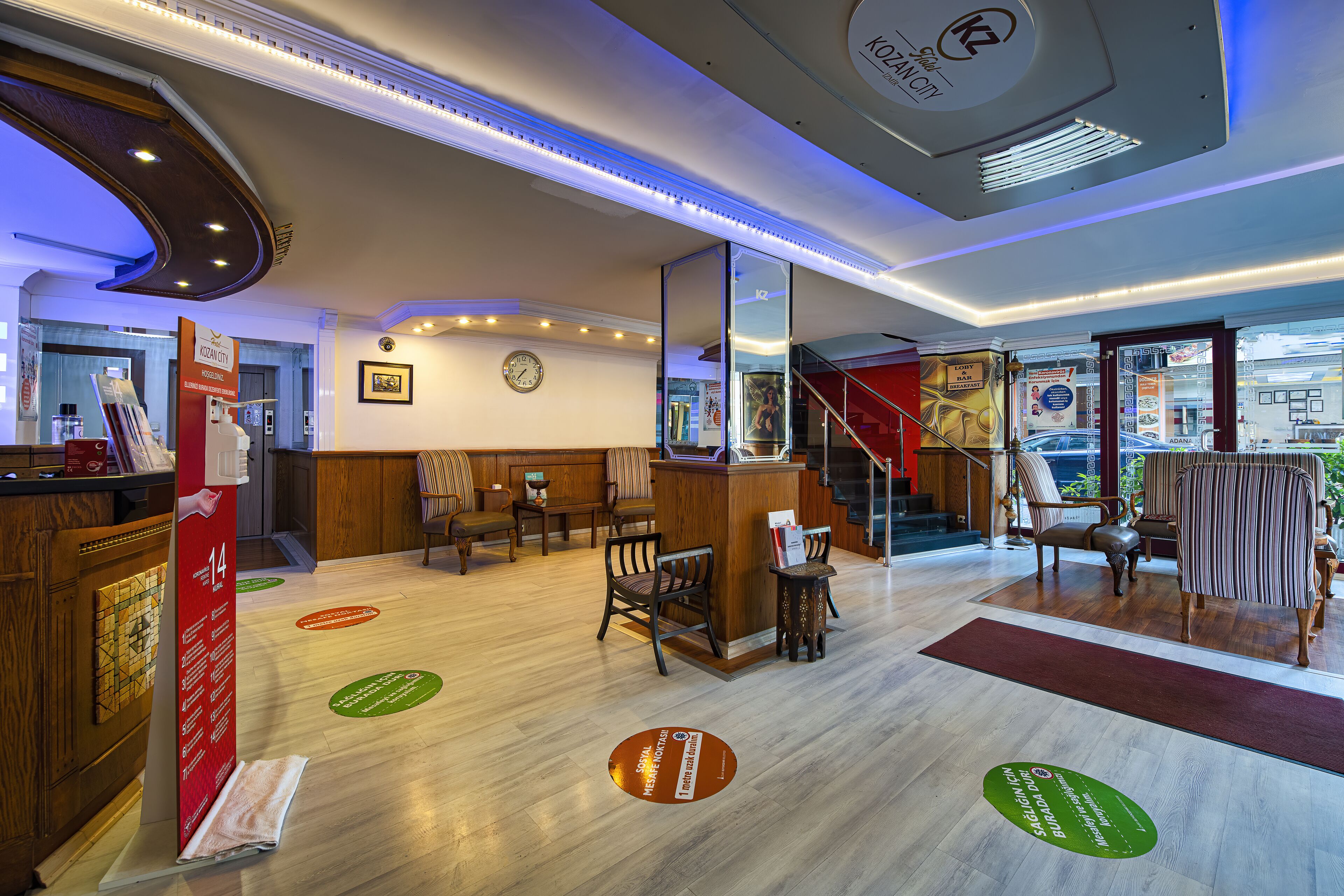 A hotel lobby with a reception desk, seating area, and a staircase leading to an upper floor.
