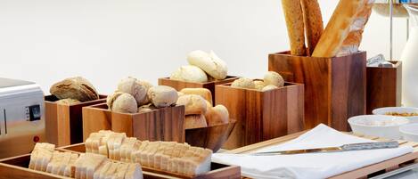 A variety of breads and pastries in wooden containers, a knife, and a bowl of jam on a table.