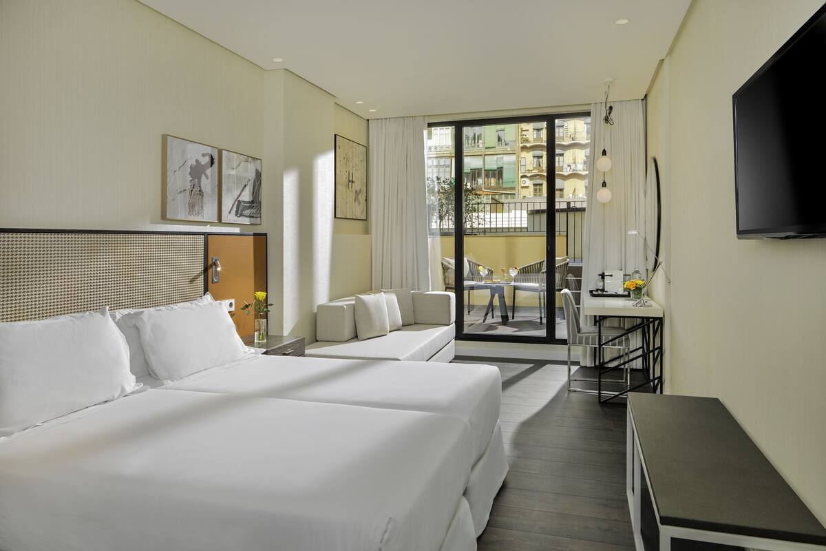A hotel room with two beds, a desk, and a view of the outside balcony.