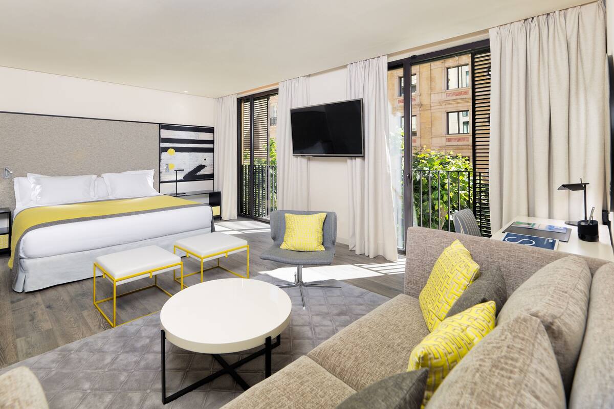 A modern hotel room with a bed, a sofa, a round table, and a TV.