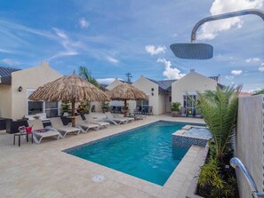 A pool area with lounge chairs, two thatched umbrellas, and a hot tub. - Golden Villas Aruba (Noord)
