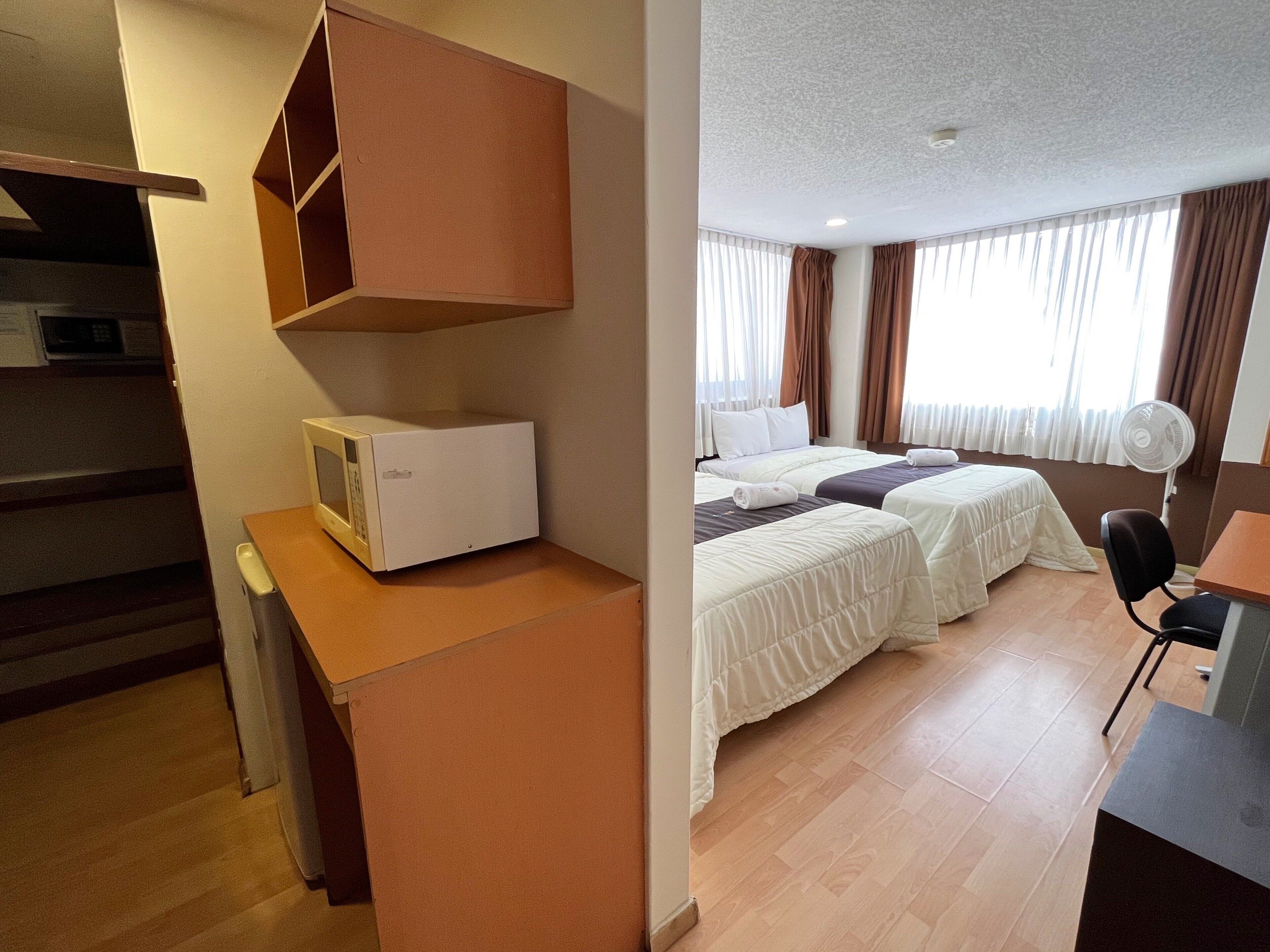 A hotel room with two beds, a microwave, a desk, and a chair.