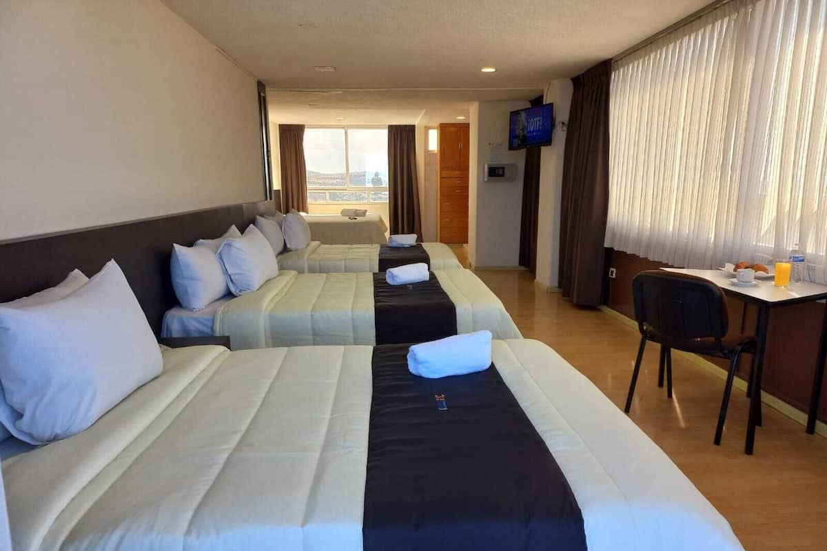 Habitación de hotel con dos camas, un escritorio con silla, televisor y ventana con cortinas.