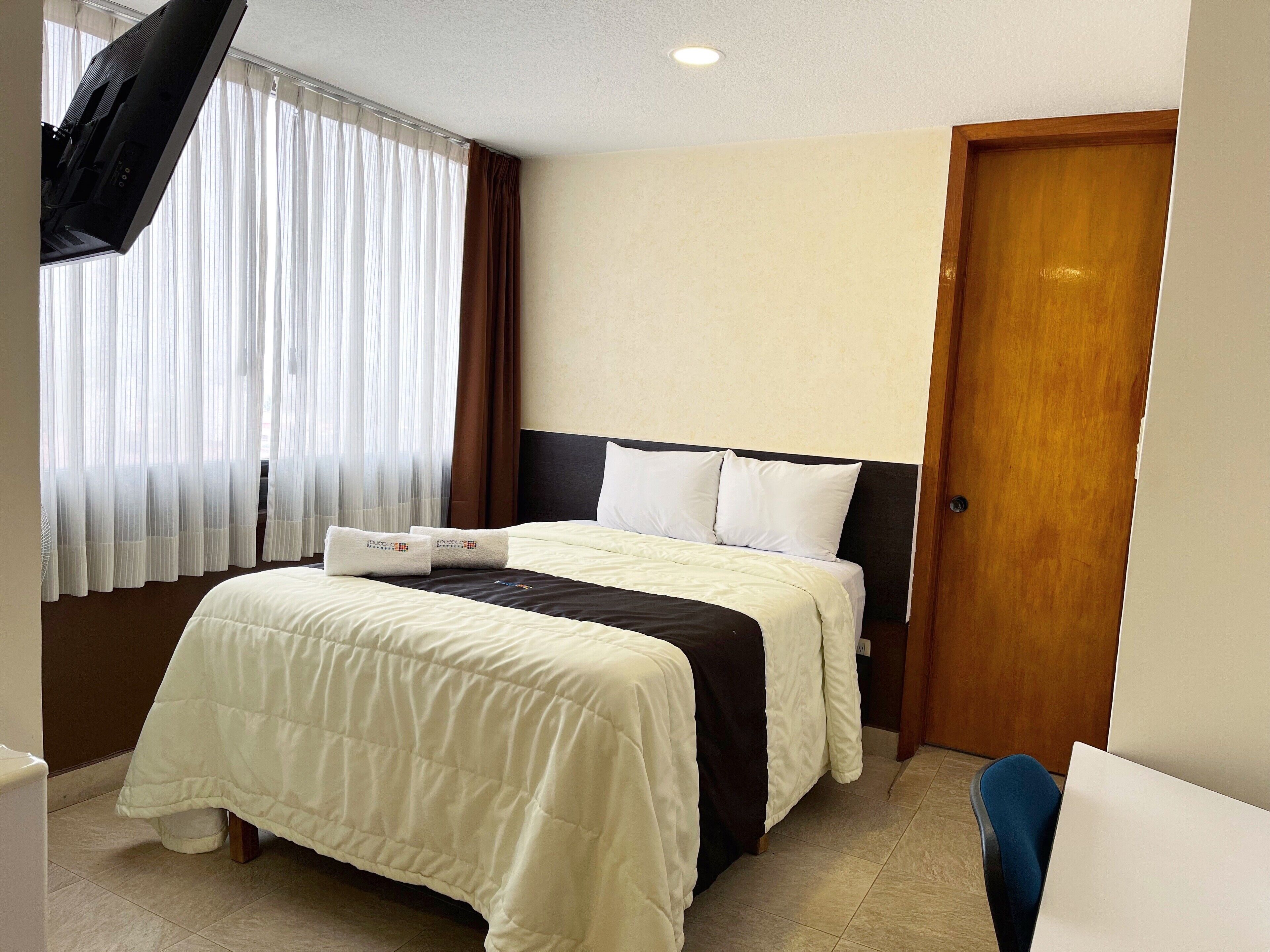 Una habitación de hotel con cama, una puerta de madera y ventana con cortinas.