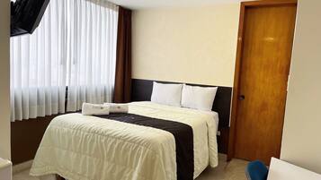 Una habitación de hotel con cama, una puerta de madera y ventana con cortinas.