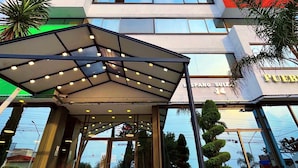 Un hotel de varios pisos con un diseño moderno, que cuenta con una entrada de vidrio y un área exterior cubierta.