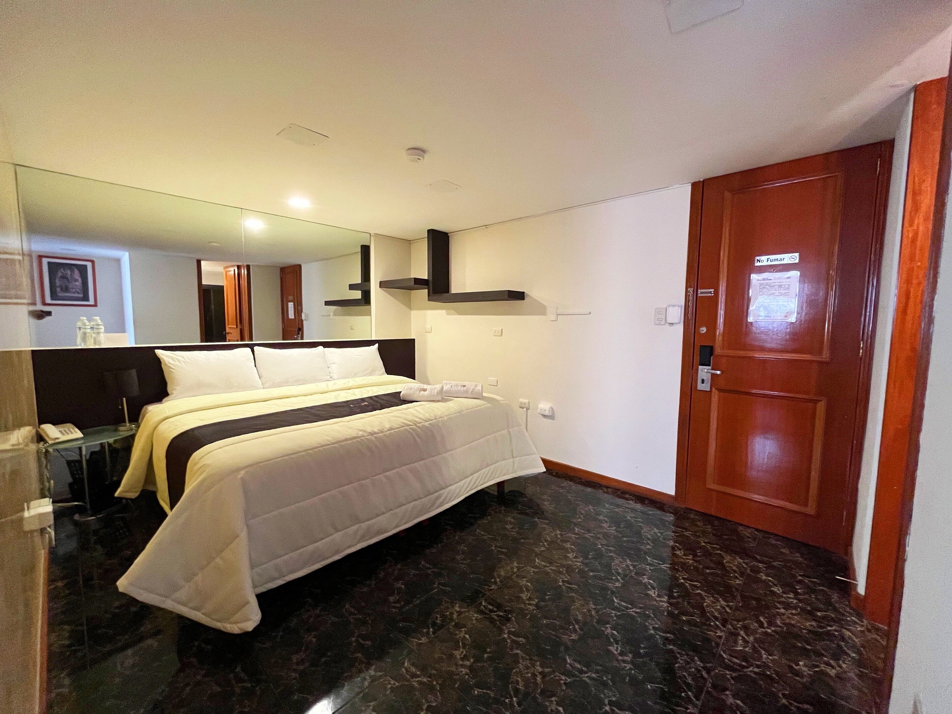 A hotel room with a bed, a wooden door, a mirror, and a marble floor.
