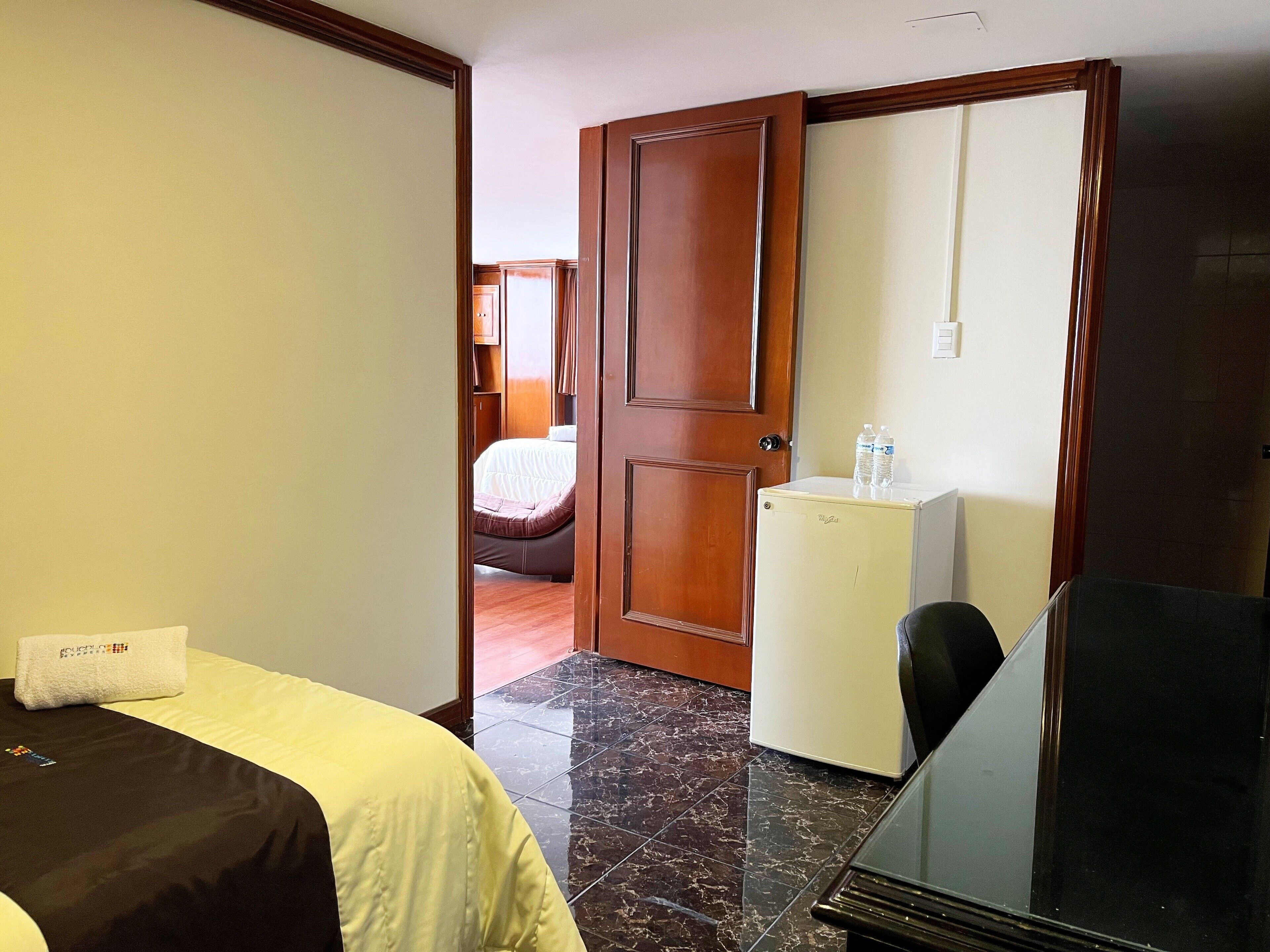 A hotel room with a bed, a small refrigerator, a desk, and a chair.